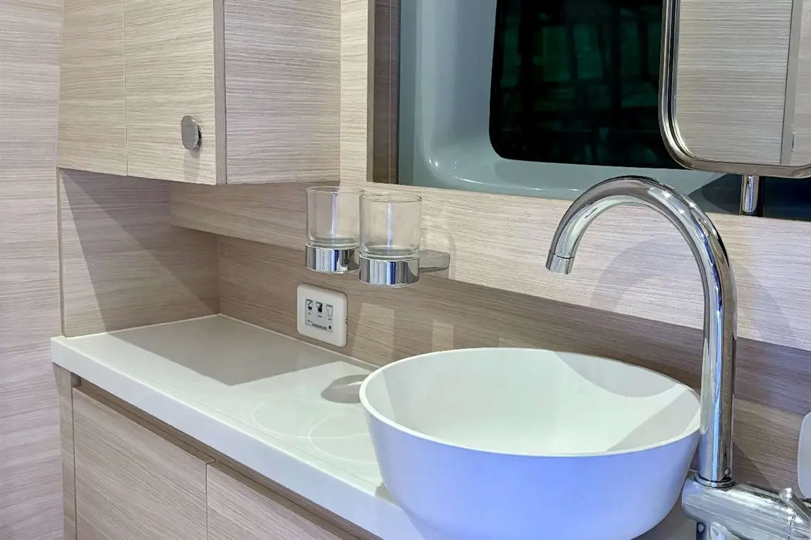 Modern bathroom sink with a sleek, white bowl, chrome tap, and two glass holders on a wooden countertop.